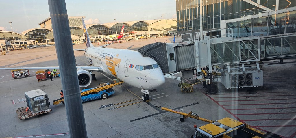 An airplane at a gate in an airport, with ground crew and luggage carts nearby.