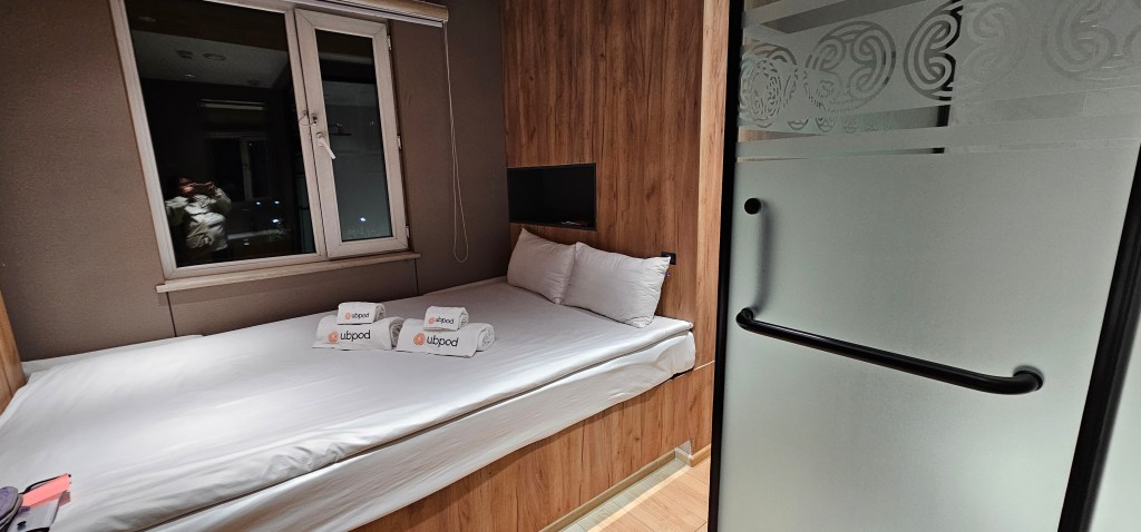 Compact hotel room featuring a single bed with white linens, a window with a view, and a television mounted on the wall.