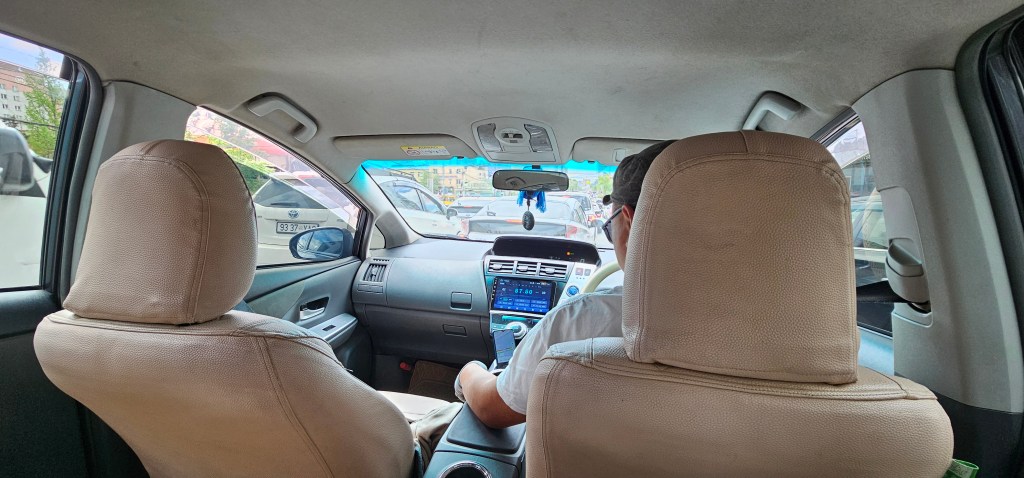 Interior view of a car showing the back of the driver's seat and passenger seat, with a focus on the dashboard and traffic outside.