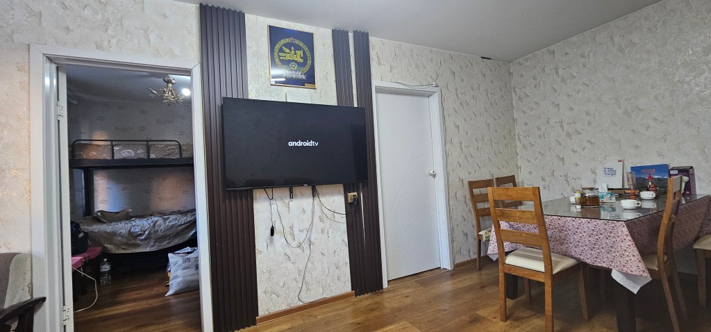 View of a living room with a television mounted on the wall, a dining table set with dishes, and a doorway leading to a bunk bed area.