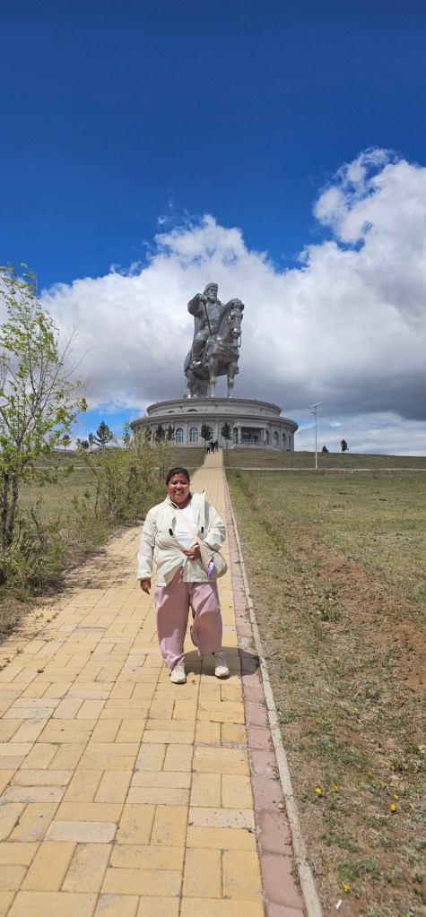 A person stands on a yellow brick pathway in front of a large equestrian statue under a blue sky with clouds.