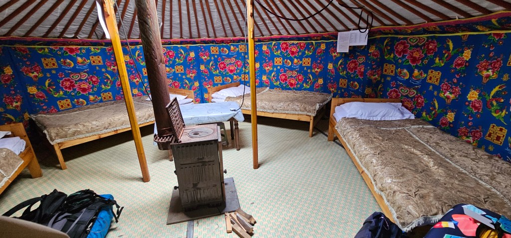 Interior of a yurt with several wooden beds and a small stove, featuring colorful floral patterned walls.