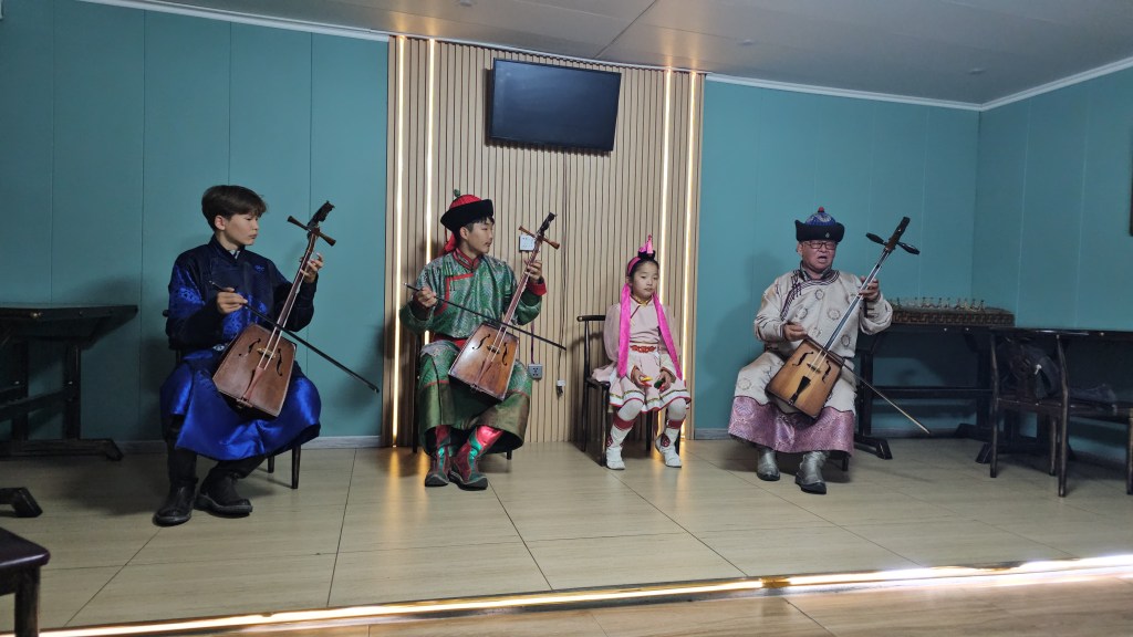 Four musicians playing traditional instruments in a cultural performance, featuring a girl in traditional attire.