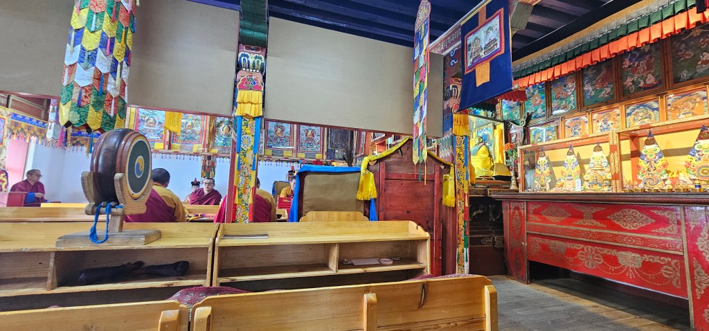 Interior of a Tibetan temple, featuring vibrant decorations, wooden benches, and monks in discussion.