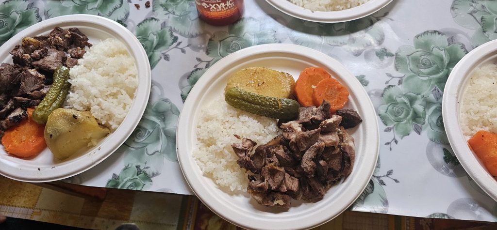 Two plates of rice with various cooked vegetables and meat, including carrots, potatoes, and green peppers, served on a floral patterned tablecloth.