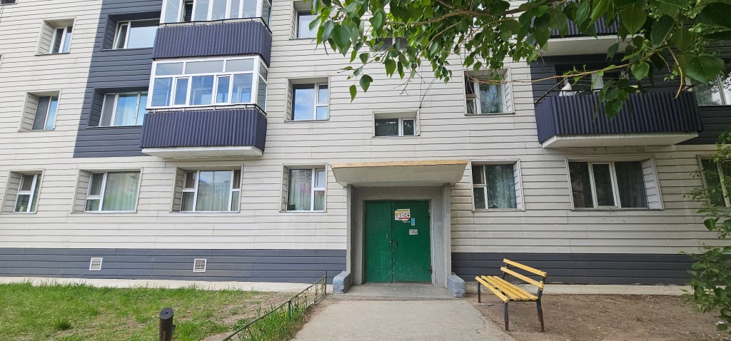 Front view of a multi-story residential building with a green entrance door and a yellow bench in the foreground.