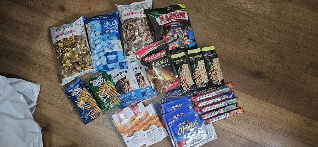 An assortment of snacks and products including various packages of candy, pretzels, coffee, and granola bars arranged on a wooden floor.