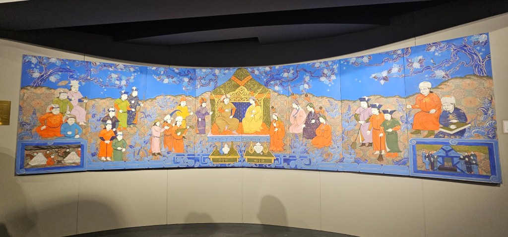 Colorful mural depicting various figures in traditional attire, surrounded by intricate patterns and nature motifs, illustrating a cultural or historical scene.