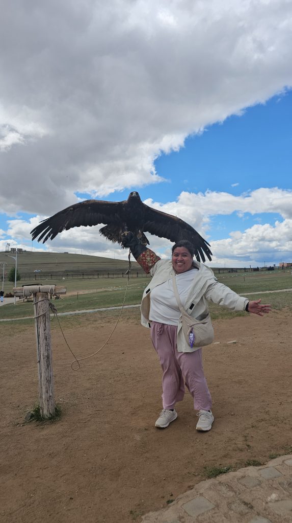 A person joyfully posing with a large eagle on their arm, set against a backdrop of blue skies and scattered clouds.