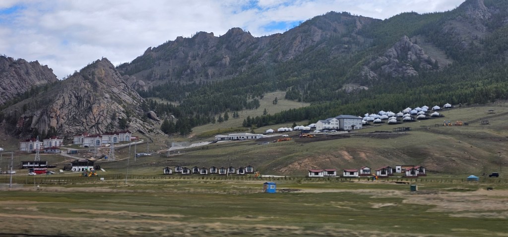 A scenic view of mountainous terrain featuring a mix of traditional yurts and modern accommodations in a green landscape.