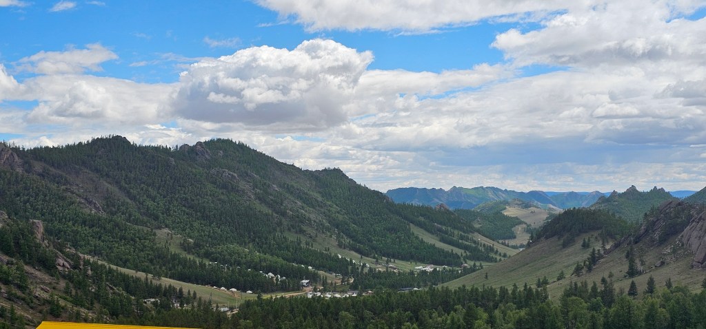 Panoramic view of lush green mountains and valleys under a cloudy blue sky.