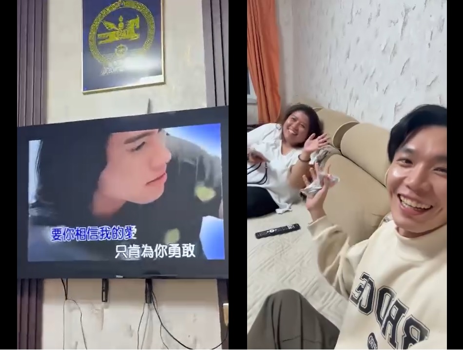 A living room scene featuring a television displaying karaoke lyrics, with two people seated on a couch, one smiling and waving, while the other appears happy and engaged.