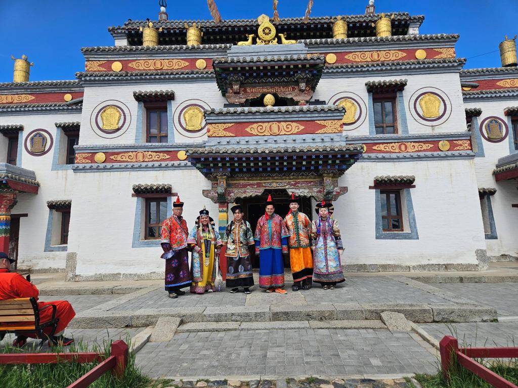 Group of individuals in traditional attire posing in front of a colorful ornate building.